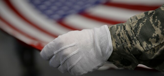 A new honoe guardsman practices folding a flag while wearing gloves at Mountain Home Air Force Base, Idaho, March 3, 2016. Honor guard's top priority is to make sure fallen veterans are rendered proper military honors. (U.S. Air Force photo by Senior Airman Jessica H. Evans/RELEASED)