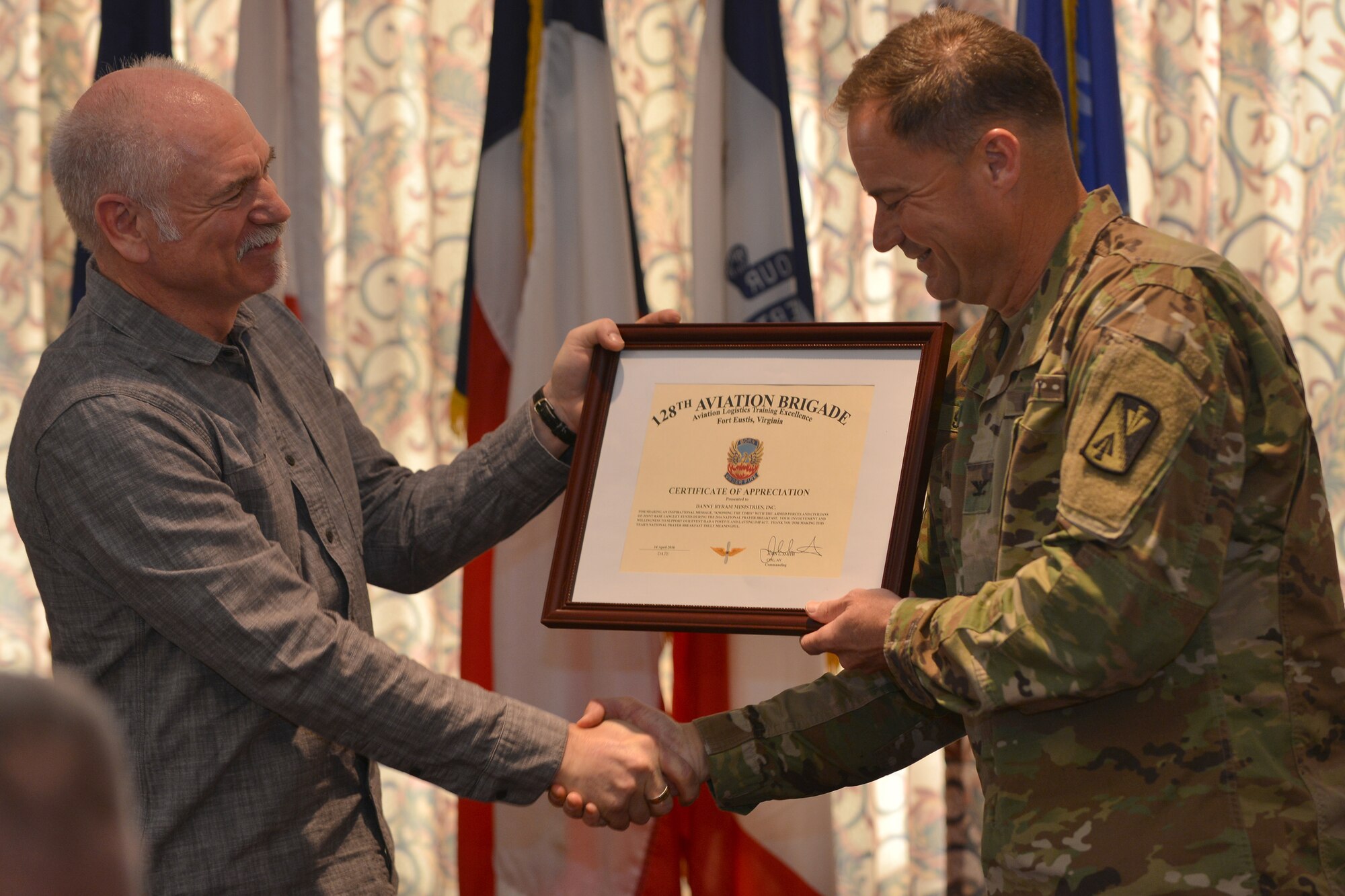 U.S. Army Col. John Smith, the commander of the 128th Aviation Brigade, gifts a certificate of appreciation to Danny Bryam, guest speaker, during the National Prayer Breakfast at Fort Eustis, Va., April 15, 2016. Bryam not only gave a speech during the event, but also performed songs of worship for the breakfast attendees. (U.S. Air Force photo by Staff Sgt. Natasha Stannard)