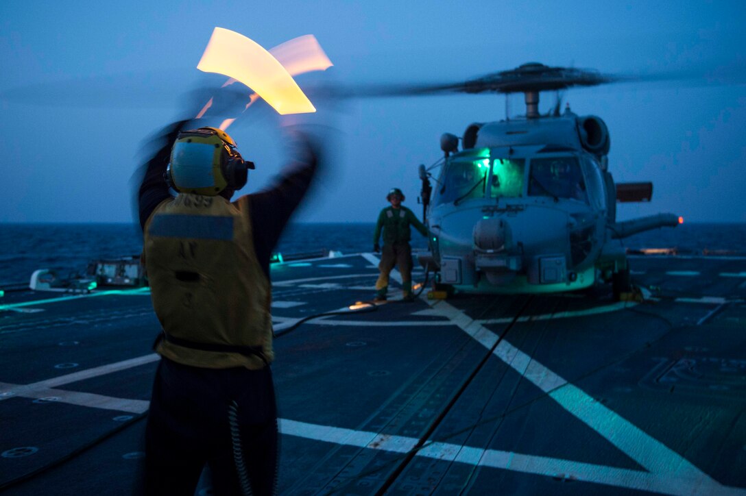 Combat Operations: A sailor signals to an MH-60R Sea Hawk helicopter during flight quarters in the Arabian Gulf, April 29, 2015. The sailor is assigned to the guided-missile destroyer USS Farragut, which is supporting Operation Inherent Resolve in the U.S. 5th Fleet area of operations. The aircraft is assigned to the Grandmasters of Helicopter Maritime Strike Squadron. Navy photo by Petty Officer 3rd Class Jackie Hart