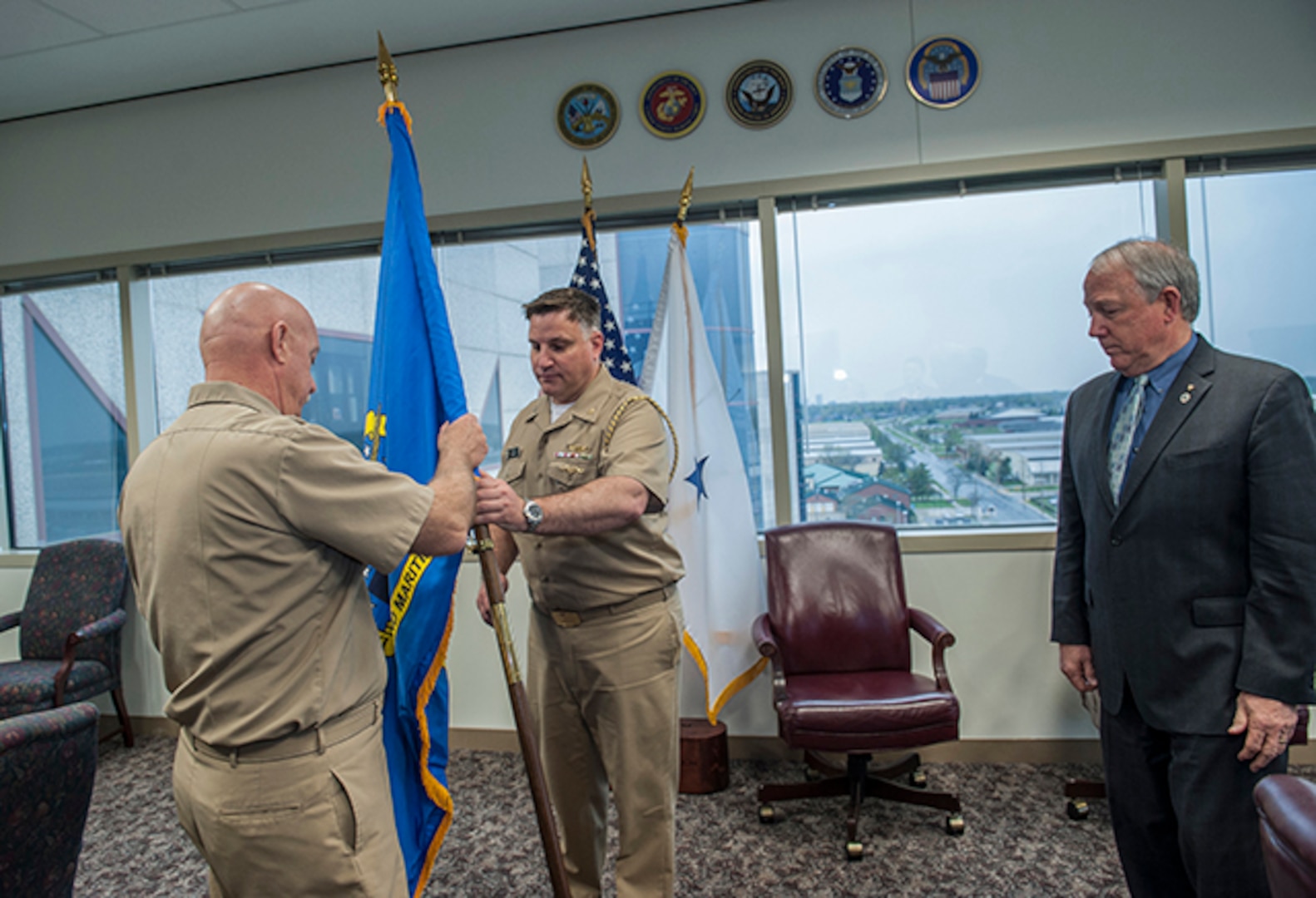 Navy Rear Admiral John King passes the organization’s flag to Navy Capt. Justin Debord, chief of staff, as he relinquishes command of DLA Land and Maritime to James McClaugherty (right). McClaugherty will serve as acting commander until the newly-identified Navy Rear Admiral Michelle Skubic arrives on station. 