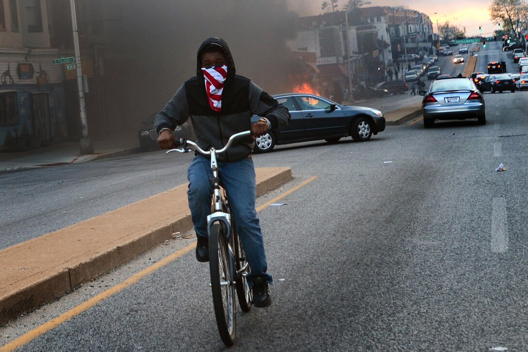 News: A young boy rides his bike away from a car that was set on fire during a riot that broke out after the funeral of Freddie Gray in Baltimore, April 27, 2015. Gray died April 19 from a severe spinal injury that allegedly occurred while in police custody. Looting and riots broke out in Baltimore after the funeral. The Maryland governor declared a state of emergency. Air Force photo by Staff Sgt. Kenny Holston