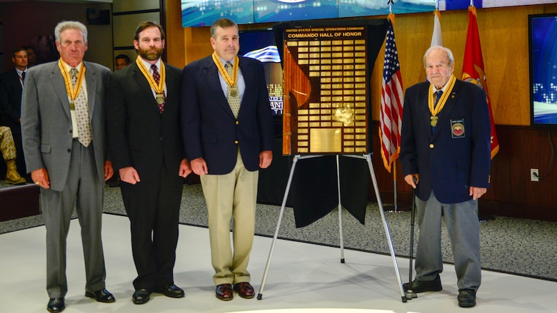 (From left to right) Air Force Col. Billy "Rusty" Napier, Marine Corps Master Sgt. John Mosser, and Marine Corps Col. Robert Coates, and Army Maj. Caesar Civitella, stand next to the Commando Hall of Honor display after they were inducted into the USSOCOM Commando Hall of Honor during a ceremony held at USSOCOM headquarters, on MacDill Air Force Base, Fla., April 20. Not pictured, but inducted, is Army Maj. Thomas Powell who attended the ceremony via video teleconference. 