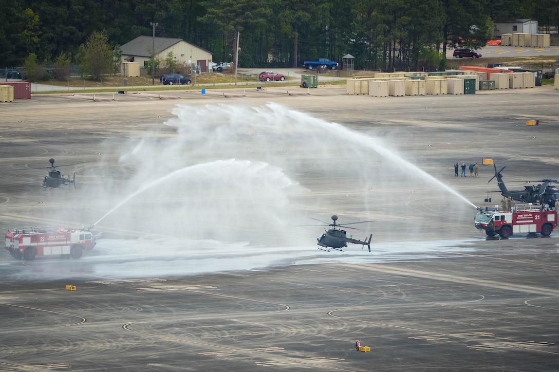 An OH-58 Kiowa Warrior helicopter is showered by an arch of water from fire trucks following the final formation flight at Simmons Army Airfield, N.C., April 15, 2016. DoD photo by Kenneth Kassens