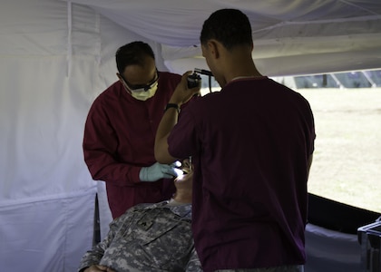 A dentist and his assistant with 145th Multifunctional Medical Brigade, an Army Reserve unit from Garden Grove, California, perform and oral exam on a Soldier with 17th Field Artillery Brigade, 7th Infantry Division, during a total force integrated training exercise at Joint Base Lewis-McChord, Washington, April 18-29, 2016. The 145th MFMB provided basic dental services out of three tents as part of the exercise. (U.S. Army photo by Sgt. Cody Quinn/28th Public Affairs Detachment)