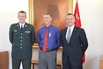 Capt. Bradley Grimm, center,Texas Army National Guard, receives the Danish Defense Medal for Special Meritorious Efforts by Danish Defense Gen. Peter Bartram, left, and American ambassador to Denmark Rufus Gifford, right, at a ceremony held in Denmark, April 19, 2016.  Grimm was instrumental in foiling a terrorist plot to bomb a Danish school and assisted Danish security forces in making an arrest. (Danish Military photo by Sune Wadskjær/Released)