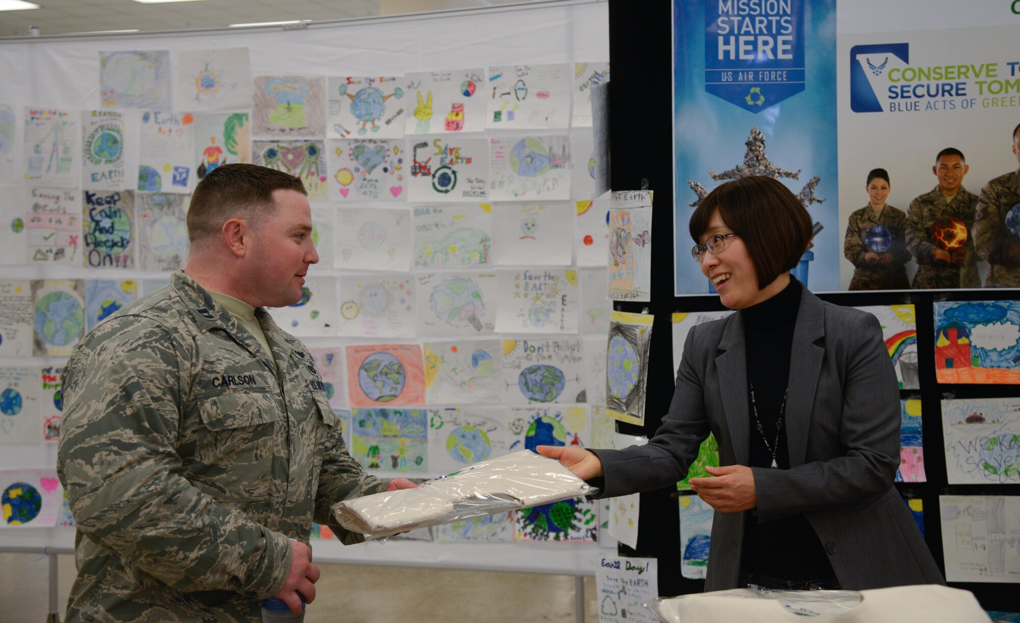 Capt. Kurt Carlson, 51st Fighter Wing crisis action team director, accepts a cotton grocery bag from Sin, Yun O, 51st Civil Engineer Squadron environmental specialist, during an Earth Day booth event at the base exchange April 19, 2016, at Osan Air Base, Republic of Korea. The 51st CES gave out cotton bags to encourage Osan members to recycle. (U.S. Air Force photo by Senior Airman Dillian Bamman/Released)