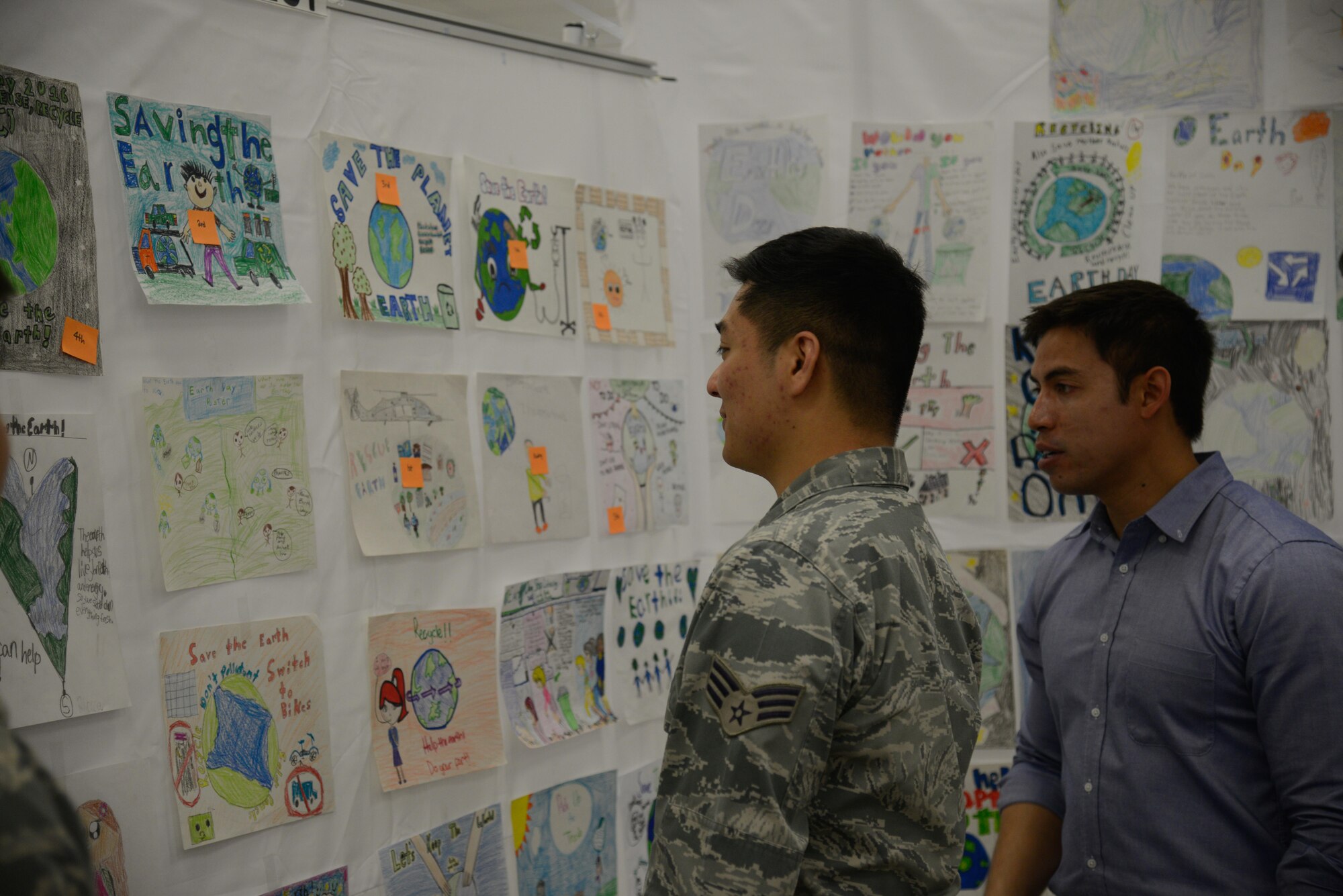 Senior Airman Dan Doan, 51st Civil Engineer Squadron engineering technician, and Matthew Tubtim, 51st CES fuel tank and water quality manager, look at Earth Day posters during an Earth Day booth event at the base exchange April 19, 2016, at Osan Air Base, Republic of Korea. Team Osan children drew the posters to highlight saving the environment for Earth Day. (U.S. Air Force photo by Senior Airman Dillian Bamman/Released)