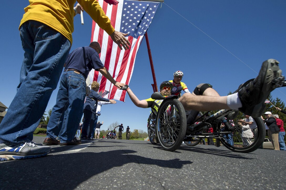 Former Navy Petty Officer 1st Class Jay Somers, right, gives high-fives as he passes through a cheering crowd along the Face of America bike route in Gettysburg, Pa., April 24, 2016. More than 150 disabled veteran cyclists and 600 other cyclists rode 110 miles from Arlington, Va., to Gettysburg, Pa., over two days to honor veterans and service members who were wounded or disabled while serving the nation. DoD photo by EJ Hersom