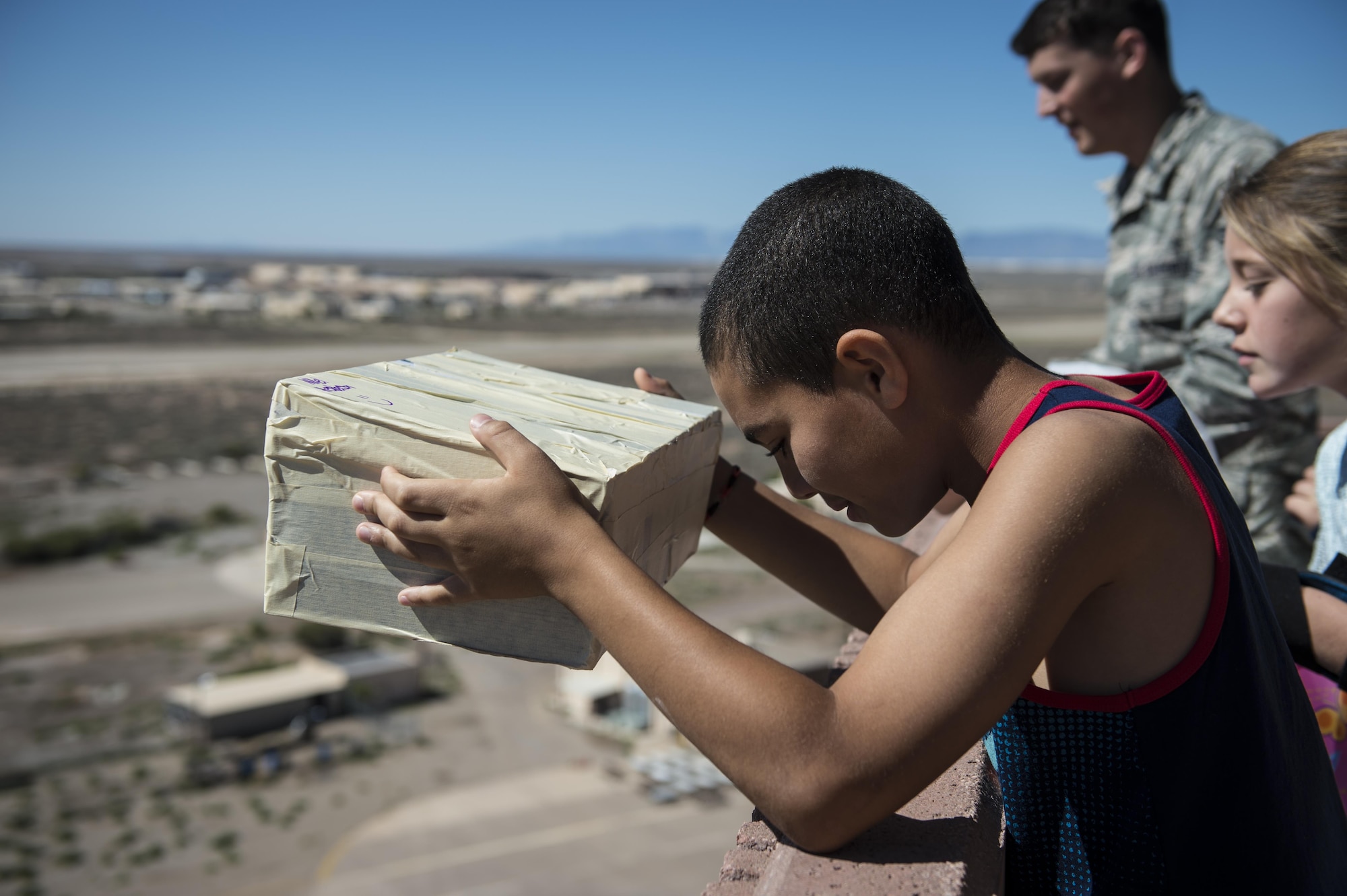 A student from the Holloman Elementary School aims his egg protected by a box as part of an egg drop science project at the Holloman Air Force Base air traffic control tower here, April 14. The egg drop project challenges students to create a contraption that will keep an egg safe from impact after being dropped from a tall building, in this case, 14 stories. Typically eggs are dropped from the participating school’s roof. Holloman students had the unique opportunity to utilize the air traffic control tower for this project. (U.S. Air Force photo by Senior Airman BreeAnn Sachs)