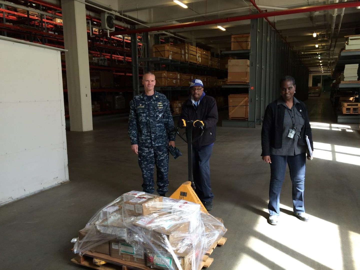 DLA Distribution Norfolk’s commander Navy Capt. Harry Thetford, left, poses with Charles Elley, center, and Cheryl Harris, right, with the initial Regional Maintenance Center materials being stored at the distribution center.