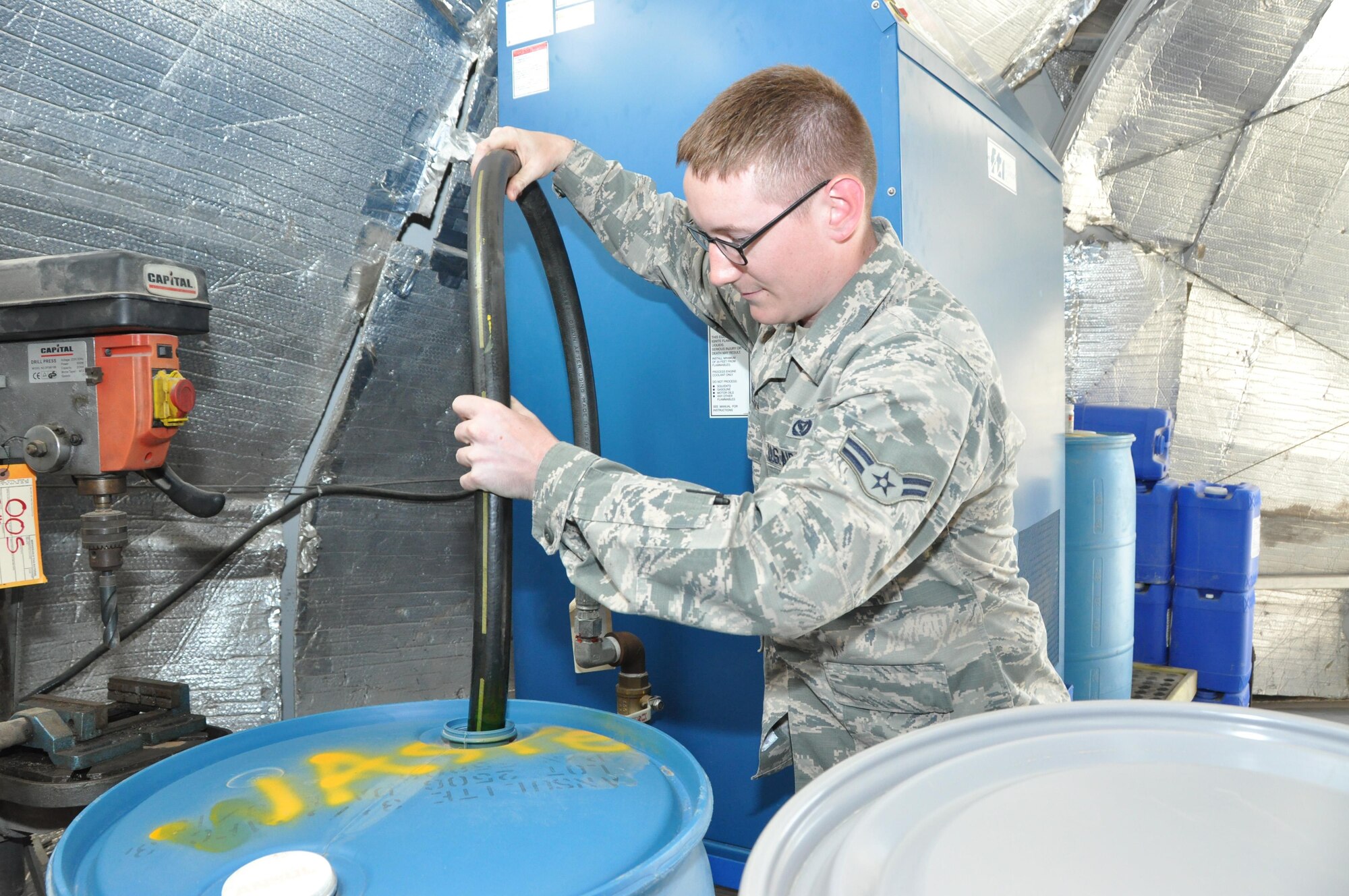 Airman 1st Class Tyler, 380 Expeditionary Civil Engineer Squadron crewmember, inserts a hose into a 55 gallon drum full of used coolant here 20 Apr. 2016. The coolant reclaimer returns 60 percent of recycled fluid, which is used to power generators in direct support of the mission. (U.S. Air Force photo by Staff Sgt. Samantha Mathison)