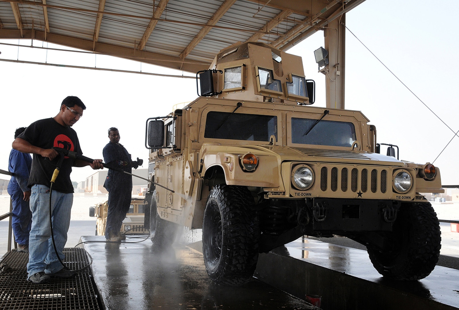 Ram Chhetri, a mechanic from Nepal, washes off an M1151 up-armored Humvee outside the 1st Battalion, 401st Army Field Support Brigade vehicle maintenance facility at Camp As Sayliyah, Qatar, Oct. 8. Ray Green, a mechanic from Charleston, S.C., supervises from behind the vehicle. Shipped from Iraq, ITT-contracted mechanics finished retrofitting the vehicle to Fragmentation Kit Seven configurations, upgrading it from FRAG-5.