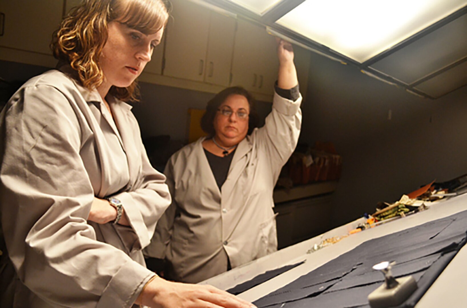Defense Logistics Agency Product Testing Center color scientists Ardra Farally (left) and Jamie Hieber analyze a fabric sample against Coast Guard uniform standards and tolerances in the center's color shading laboratory. The two conduct color science testing on every piece of fabric the military buys through DLA Troop Support's clothing and textiles supply chain.