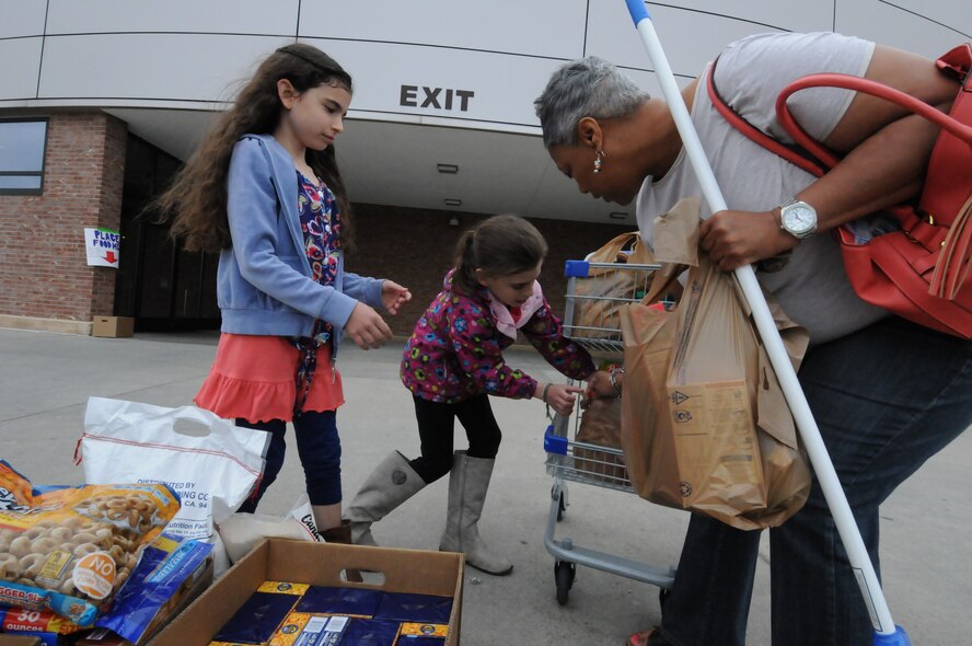 Alaina and Abrielle Janaros gather donations from Valerie Decoursey during a Kids Helping Kids donation event at the commissary on Peterson Air Force Base, Colorado, Saturday, April 23, 2016. Schriever families held the drive for the Ellicott Helping Hands Food Pantry. (U.S. Air Force photo/2nd Lt. Darren Domingo)