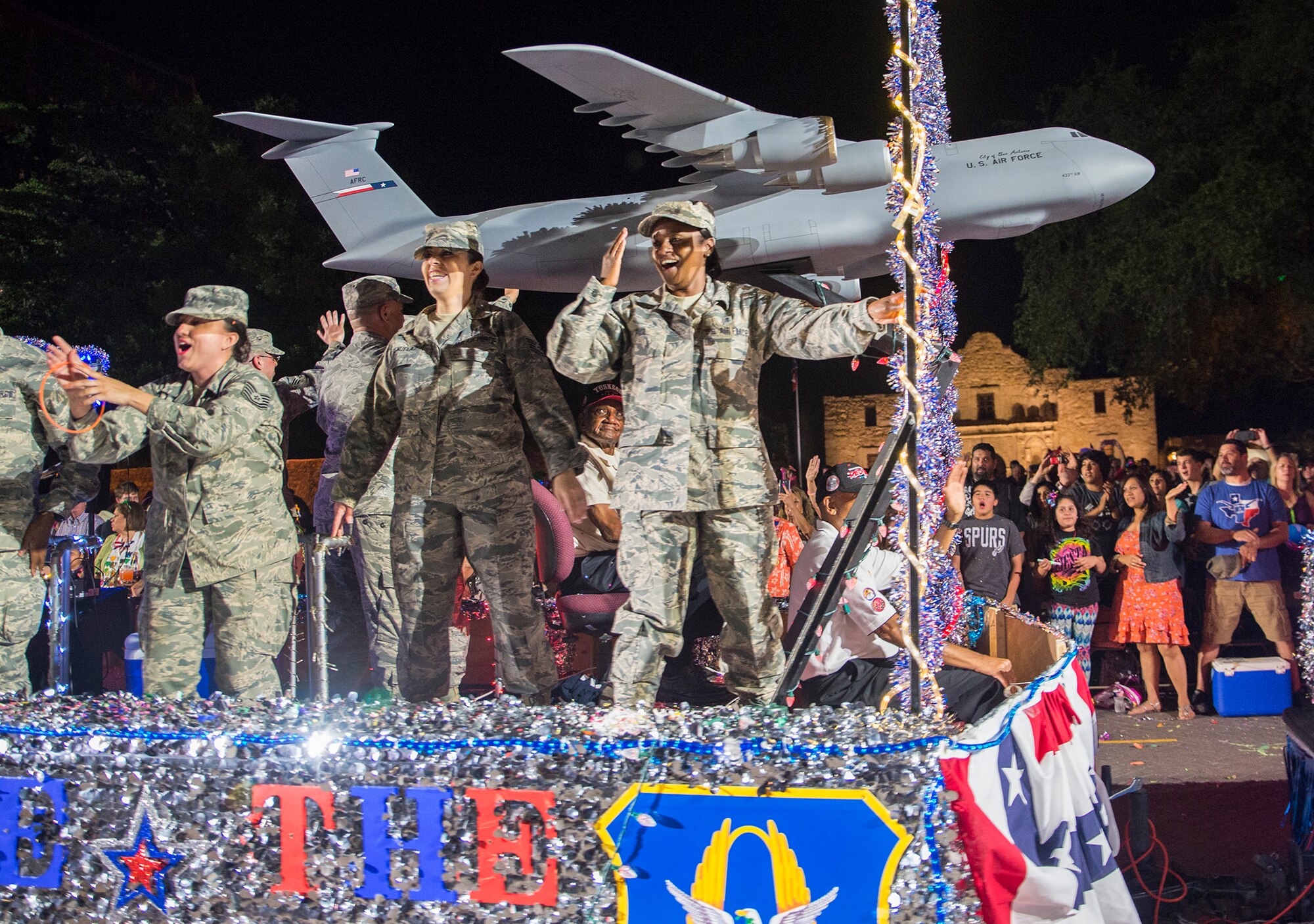 Airmen with the 433rd Airlift Wing wave to the grandstands as they pass in front of the Alamo during the Fiesta Flambeau parade April 23, 2016. The Fiesta Flambeau parade is one of the largest illuminated parades in the world, with over 750,000 spectators and 1.5 million television viewers.  (U.S. Air Force photo by Benjamin Faske) (released)