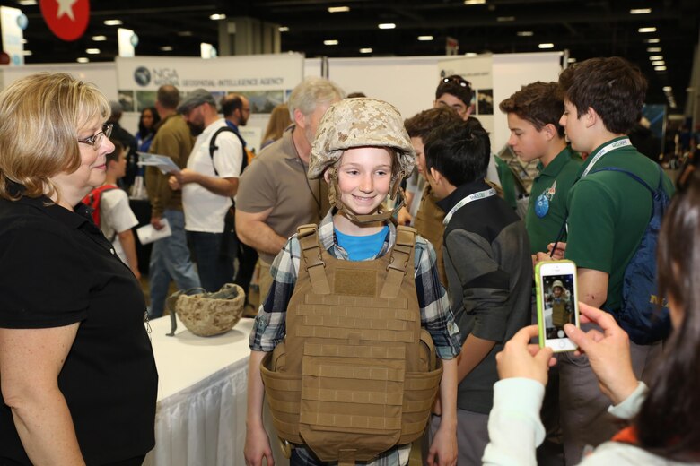 Kathy Halo (left), a safety engineer with Marine Corps Systems Command’s Infantry Weapons Systems, watches as a young attendee tries on a Marine Corps helmet and protective vest during the USA Science & Engineering Festival April 14–17 in Washington, DC. This year marked MCSC’s second year participating in the festival as part of an ongoing effort to partner with other government agencies, academic institutions and private industry to improve STEM education in the United States.  (U.S. Marine Corps photo by Mathuel Browne)