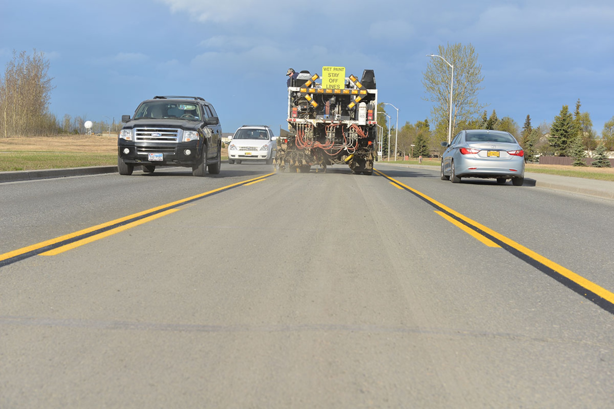A 773rd Civil Engineering Squadron paint shop striping truck lays down lines on Arctic Warrior Drive while motorists pass on either side. Passing the paint crew is not authorized if they are in the same lane, but in this case the truck is in the turn lane, so motorists should exercise caution when driving by. (U.S. Air Force photo by Airman 1st Class Kyle Johnson)