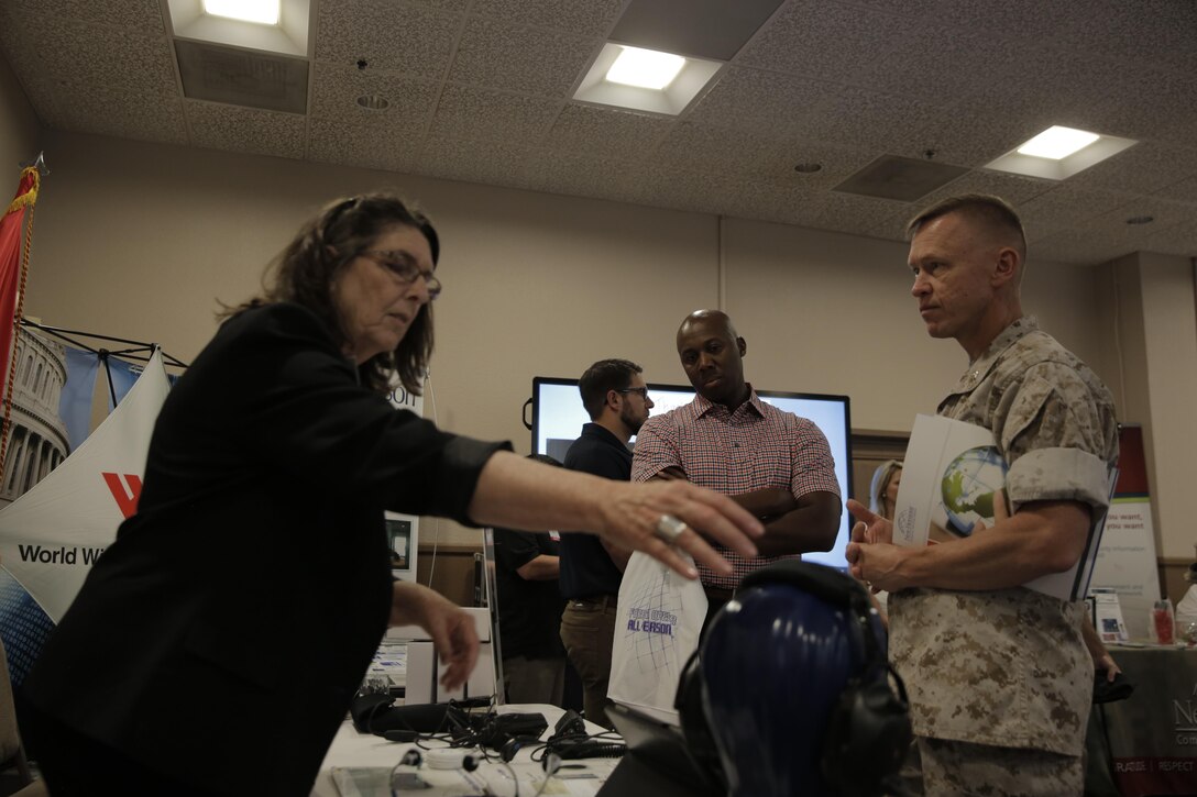 Jill DeVos, human resources, UmeVoice Inc., shows Lt. Col. Chris Dalton, academic department head, Marine Corps Logistics Operations Group, different communication equipment at the Officers’ Club during the Tactical and Technology Day Expo April 19, 2016. (Official Marine Corps photo by Pfc. Dave Flores/Released)