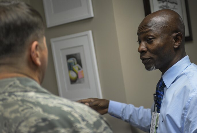 Dr. Anakwa, 99th Medical Operations Squadron internal medicine doctor, describes his artwork to an airman at the Mike O'Callaghan Federal Medical Center during his “An Art of An Art” exhibit at Nellis Air Force Base, Nev., April 21, 2016. The artwork hanging in internal not only serves as aesthetic images to look at while walking the halls, but it also serves as a way to better connect with patients. (U.S. Air Force photo by Airman 1st Class Kevin Tanenbaum)