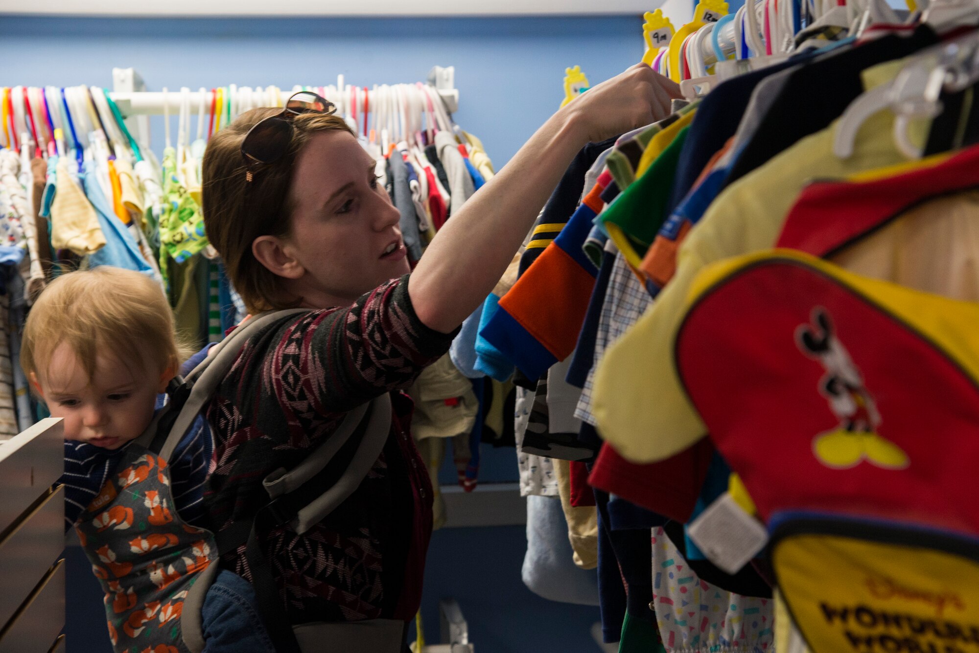 A shopper looks through clothing racks at the Chief Master Sgt. Gene Collins Airman’s Attic April 12, 2016 at Scott Air Force Base, IllThe Airman’s Attic not only serves military members E-5 and below, but they also serve their dependents. (U.S. Air Force photo by Airman 1st Class Gwendalyn Smith)