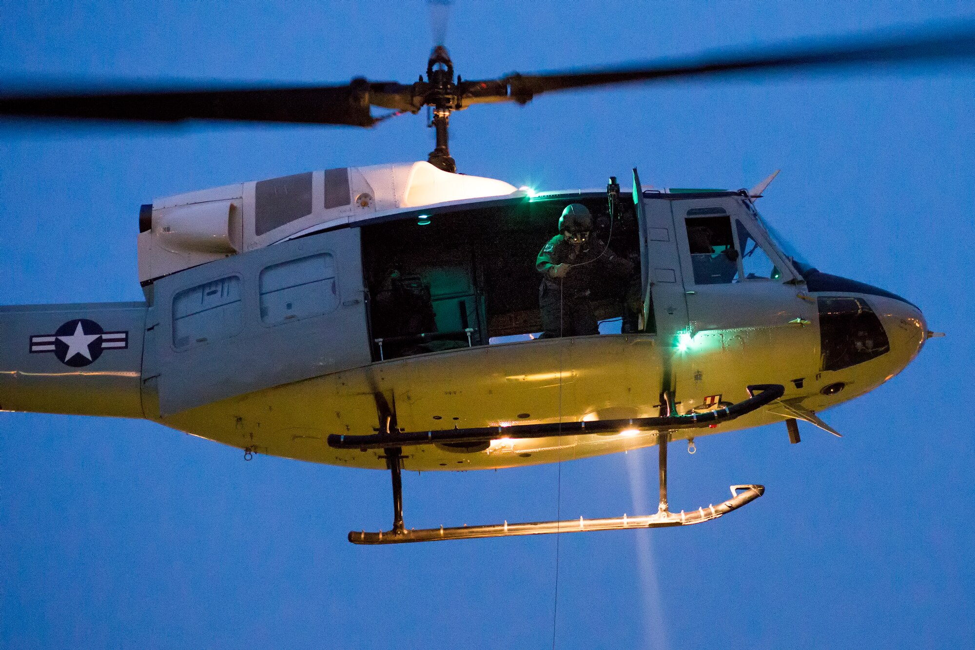 Tech. Sgt. Christopher Rector, 459th Airlift Squadron UH-1N Iroquois special missions aviator evaluator, lowers a hoist during a training flight over U.S. Army Garrison Yokohama North Dock, April 25, 2016. The 459 AS frequently train on a multitude of scenarios in order to stay prepared for potential real-world contingencies and operations. (U.S. Air Force photo by Yasuo Osakabe/Released)