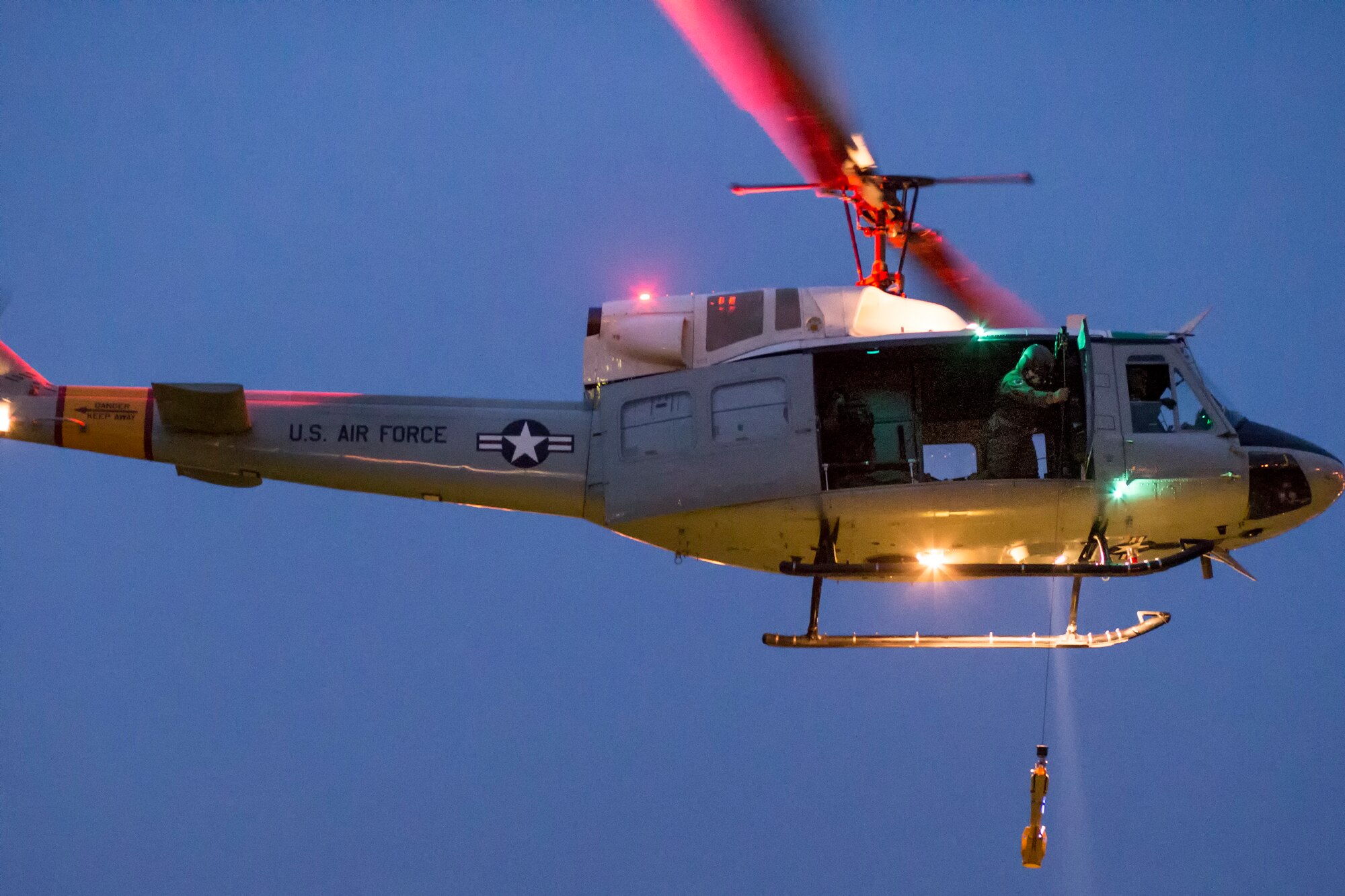 Tech. Sgt. Christopher Rector, 459th Airlift Squadron UH-1N Iroquois special missions aviator evaluator, lowers a hoist during a training flight over U.S. Army Garrison Yokohama North Dock, April 25, 2016. The 459 AS frequently train on a multitude of scenarios in order to stay prepared for potential real-world contingencies and operations. (U.S. Air Force photo by Yasuo Osakabe/Released)