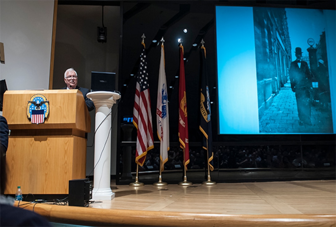 John Koenigsberg addresses an audience gathered in the Building 20 auditorium during the Defense Supply Center Columbus Days of Remembrance event. Koenigsberg shared his personal story of survival and perseverance during the Holocaust, and stressed the importance of honoring those who lost their lives by keeping their memory alive. 