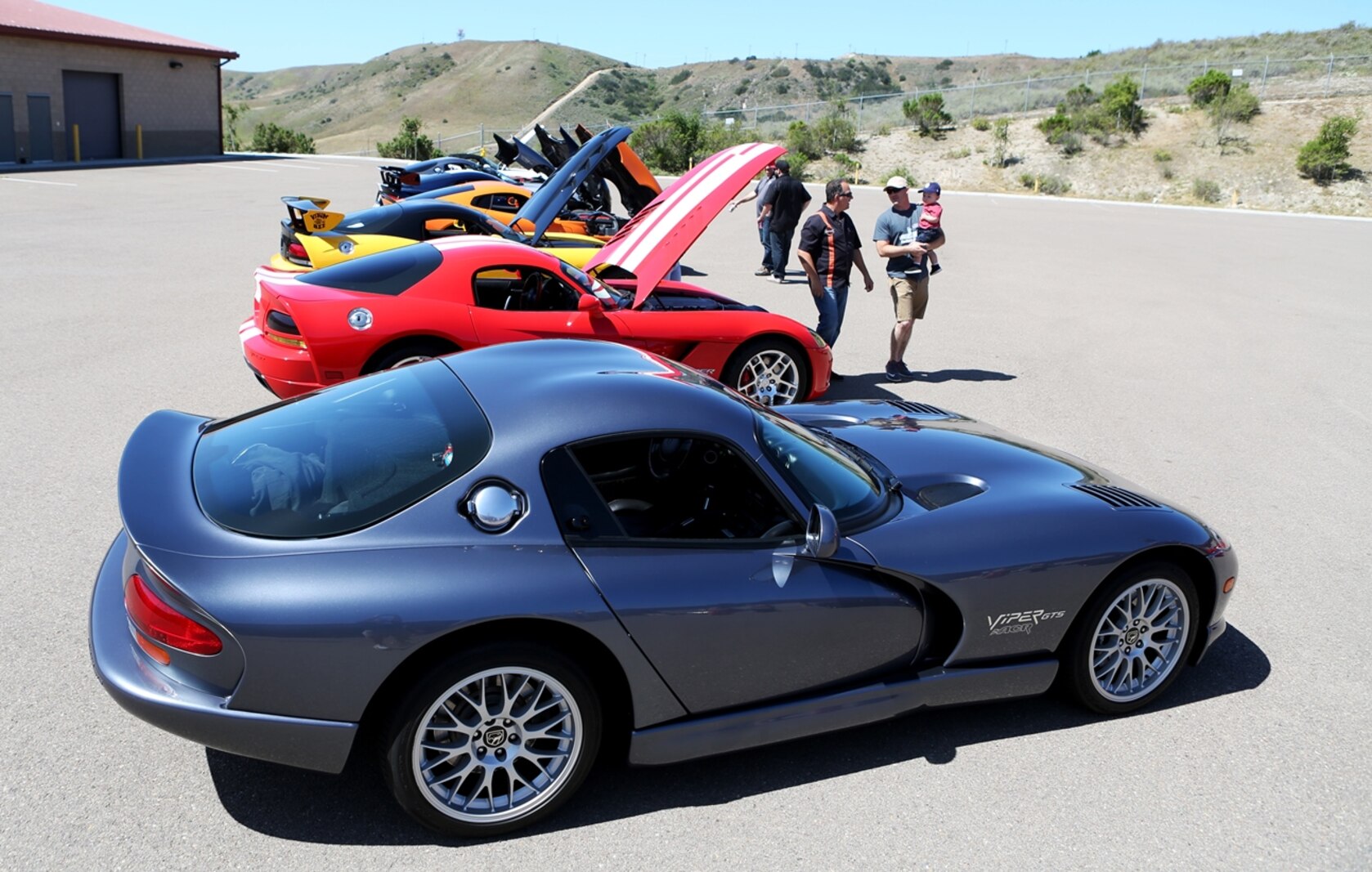 Marines and their families look at a line-up of show cars during a family day hosted by 1st Explosive Ordnance Disposal Company, 7th Engineer Support Battalion, 1st Marine Logistics Group, aboard Camp Pendleton, Calif., April 23, 2016. Marines with 1st EOD Co. hosted the Viper Club of Southern California for the day as a part of their celebration, which included food, family activities, and various show cars. (U.S. Marine Corps photo by Cpl. Carson Gramley/released)