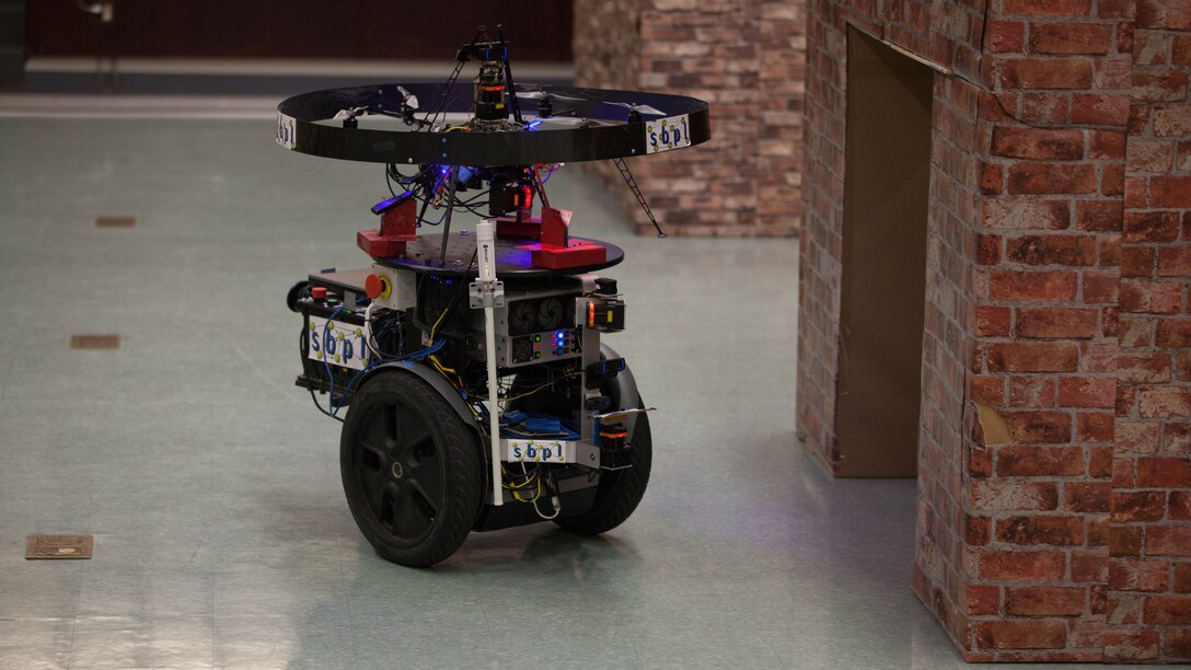 The Unmanned Tactical Autonomous Control and Collaboration patrols a simulated town indoors in Ellis Hall at Marine Corps Base Quantico, April 19, 2016. The UTACC is a team of aerial and ground robots using the Distributed Real-time Autonomously Guided Operations Engine  to provide multi-dimensional intelligence, surveillance and reconnaissance to the squad-level units. Though the tests are conceptual, the UTACC represents potential capabilities for robotics integrated into squad-level units. 