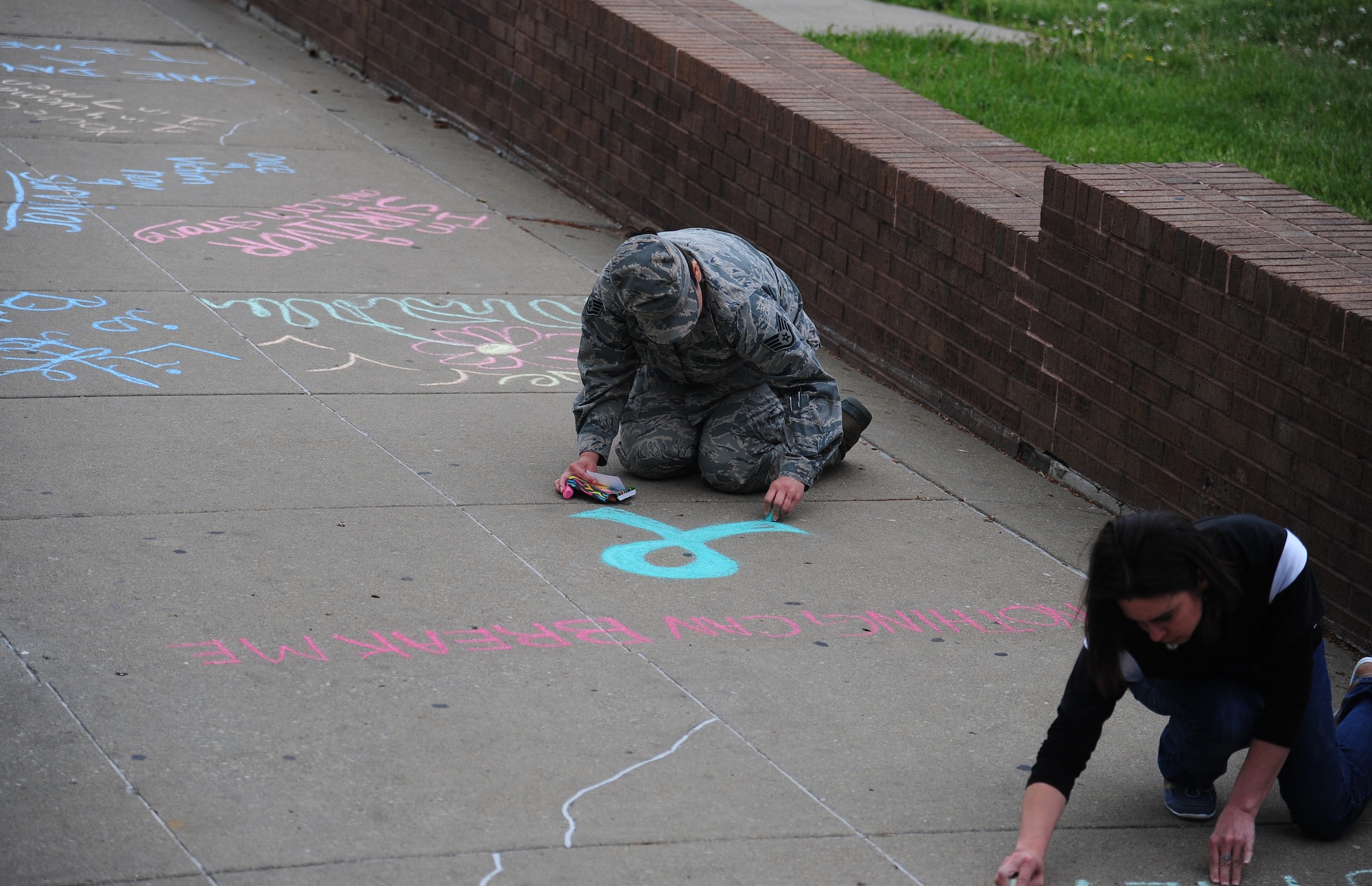 U.S. Air Force Staff Sgt. Ashley Hussain, a 509th Operations Support Squadron aircrew flight equipment craftsman, draws a Sexual Assault Prevention and Response (SAPR) ribbon in front of the Fitness Center at Whiteman Air Force Base, Mo., April 22, 2016. The SAPR team victim’s advocates wrote inspirational messages on the sidewalk in recognition of Sexual Assault Awareness Month. (U.S. Air Force photo by Senior Airman Joel Pfiester)