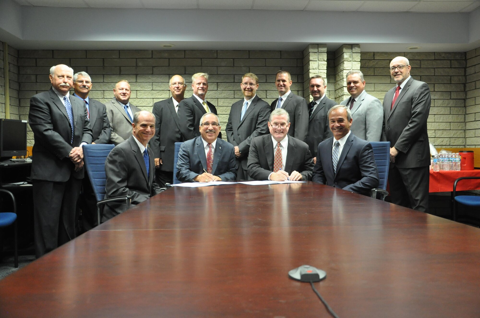 At table, from left, Dr. Kenneth W. Barker, USAF Deputy Technical Airworthiness Authority; Mr.  Jorge F. Gonzalez, USAF Technical Airworthiness Authority; Tom Hammoor, President, Textron Aviation’s defense company; nd Bill Anderson, President Textron AirLand LLC., sign the first ever Collaborative Research and Development Agreement for the Non-DoD Military Aircraft Office while surrounded by their respective team members from the NDMA office and Textron AirLand Inc. (U.S. Air Force photo/Bill Hancock)