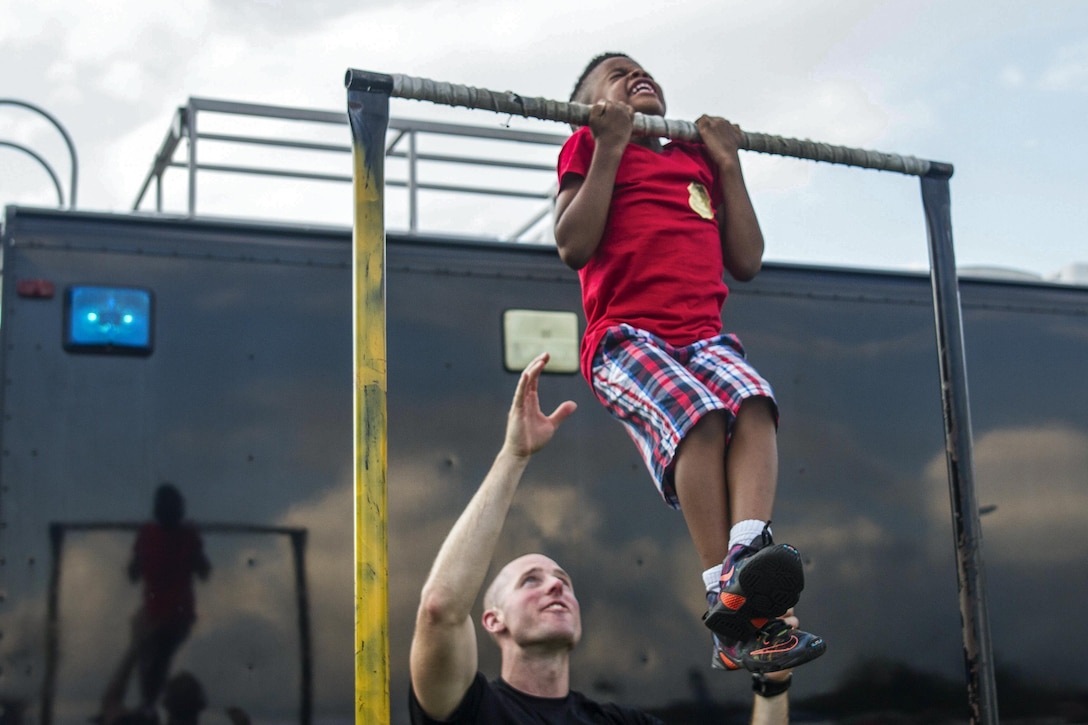 A a soldier assists a child doing pullups at the 33rd annual National Night Out at Fort Meade, Md., Aug. 2, 2016. The annual community-building campaign promotes partnerships with first-responder agencies to make neighborhoods safer. Army Reserve photo by Spc. Stephanie Ramirez