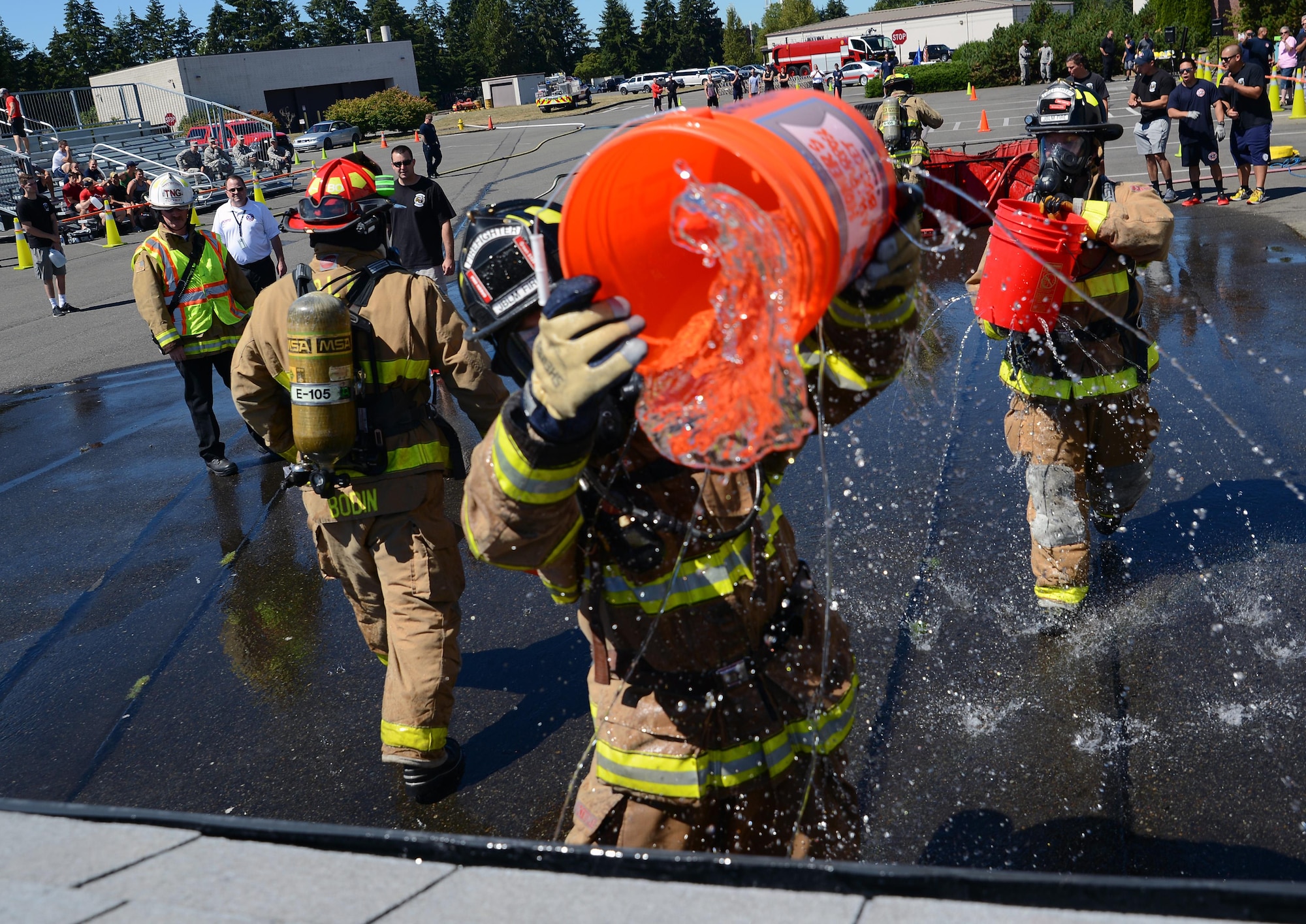 Firefighters from Fire Station 105 on McChord Field throw water onto a simulated structure fire July 26, 2016, during the firefighter combat challenge at Joint Base Lewis-McChord, Wash. This was part of a bucket brigade challenge requiring team members fill up a garbage can full of runoff water. (U.S. Air Force photo/Senior Airman Jacob Jimenez) 