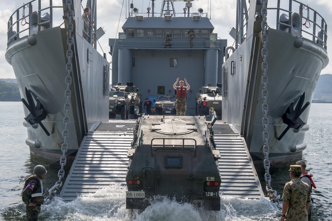 Army Spc. Michael Breneman signals to a Japanese Self-Defense Forces light armored vehicle to drive onto the USAV Coamo at U.S. Fleet Activities Sasebo, Japan, July 27, 2016. Navy photo by Petty Officer 3rd Class Kristopher S. Haley