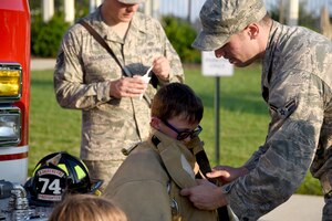 Airman 1st Class Alvaro Munarriz, 11th Civil Engineer Squadron Fire Department firefighter, assists a youth with a firefighting jacket during a National Night Out event held on Joint Base Andrews, Md., Aug. 2, 2016. The event had demonstrations from various units on base, including the 11th CES Fire Department and 11th Security Forces Squadron. (U.S. Air Force photo by Airman Gabrielle Spalding)