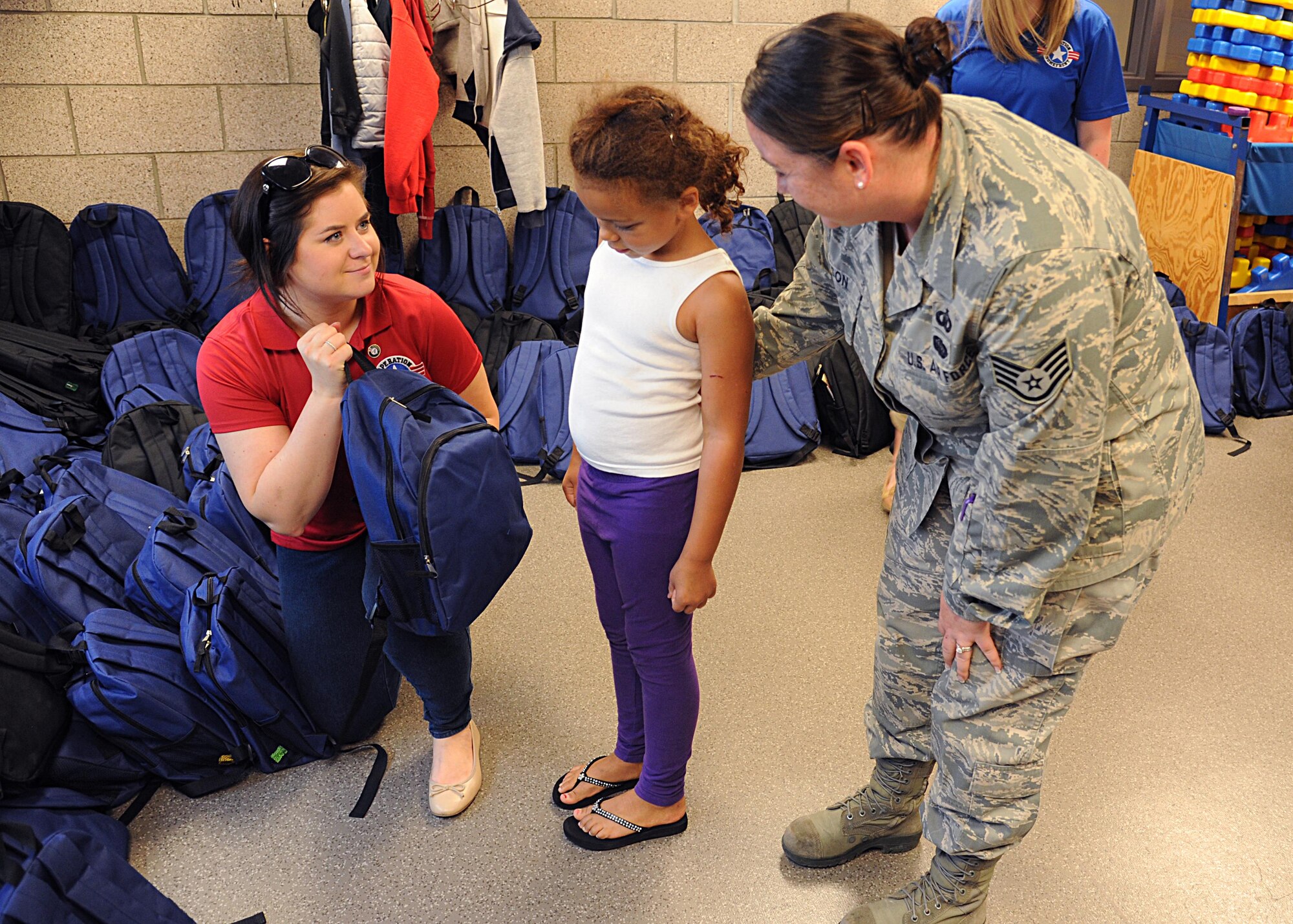 Operation Homefront volunteer Taylor Zanotti, left, hands a backpack full of school supplies to Addison Washington, 7, and her mother Staff Sgt. Angela Dotson, 319th Air Base Wing chaplain assistant, August 4, 2016, at Liberty Square on Grand Forks Air Force Base, N.D. The School Liaison Office hosted a back-to-school picnic and the Operation Homefront Back-to-School Brigade provided 200 backpacks filled with school supplies. (U.S. Air Force photo by Senior Airman Ryan Sparks/Released)