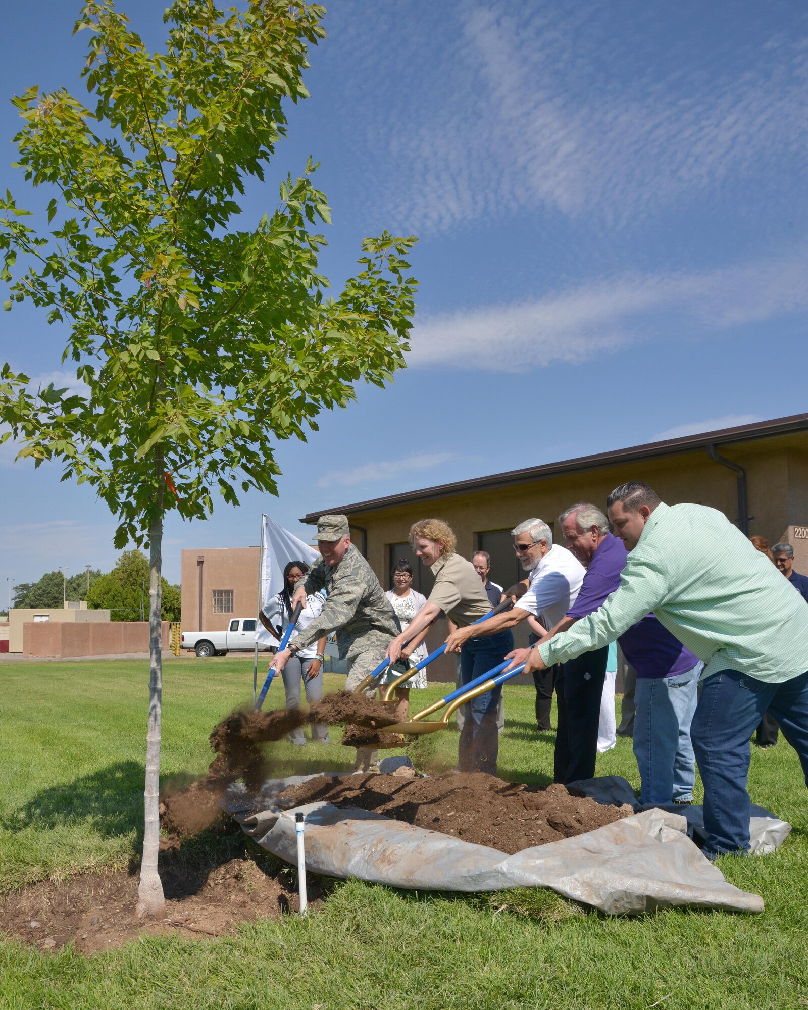 Members of the base and local communities throw the first shovelfuls of dirt soil on the new tree outside the Mountain View Club at a tree planting ceremony July 29. (Photo by Jamie Burnett)