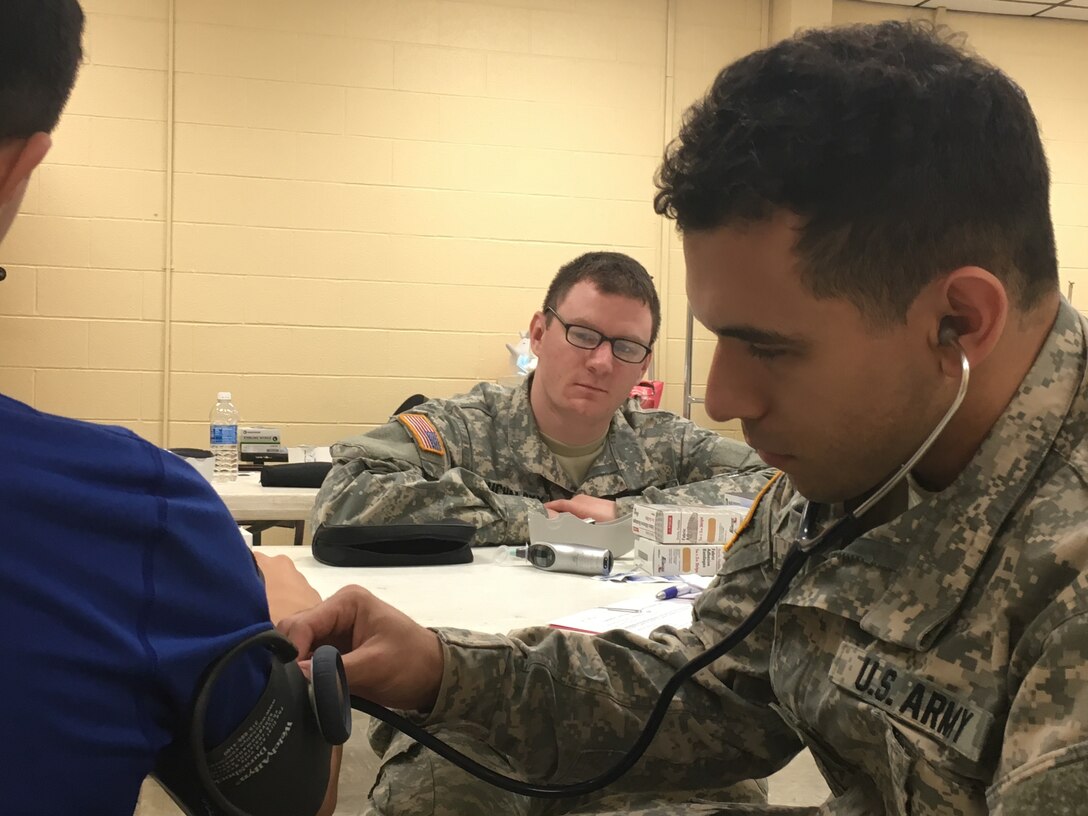 U.S. Army Reserve Pfc. Stephen Young, right, checks vitals on a patient as Sgt. Kyle Puchalsky, center, observes during Operation Lone Star at Vela Middle School in Brownsville, Texas July 25, 2016.  Both Puchalsky and Young are health care specialists with the 399th Combat Support Hospital. Operation Lone Star is one of the Innovative Readiness Training events in a joint effort between the Texas Department of State Health Services, the Texas State Guard and the U.S. Army Reserve, which provides real-world training in a joint civil-military environment while delivering world class medical care to the people of south Texas from July 25-29, 2016. (U.S. Army photo by Staff Sgt. Syreeta Shaw/released)