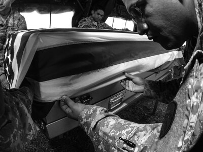 U.S. Army Reserve Spc. Anthony Hernandez with the 387th Quartermaster Company (Mortuary Affairs), based in Los Angeles, adjusts an American flag on a transfer case containing simulated human remains at the Theater Mortuary Evacuation Point, during Mortuary Affairs Exercise 16-02, July 22, at Fort Pickett, Va. MAX 16-02 included all six U.S. Army Reserve Mortuary Affairs units performing search and recovery missions and operating Mortuary Affairs Collection Points and a Theater Mortuary Evacuation Point. The units were evaluated by active-duty mortuary affairs personnel from nearby Fort Lee, Va. (U.S. Army photo by Timothy L. Hale)(Released)