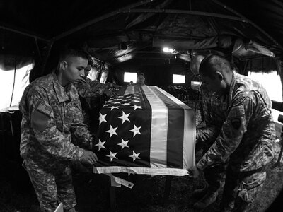 U.S. Army Reserve soldiers with the 387th Quartermaster Company (Mortuary Affairs), based in Los Angeles, place an American flag on a transfer case containing simulated human remains at the Theater Mortuary Evacuation Point, during Mortuary Affairs Exercise 16-02, July 22, at Fort Pickett, Va. MAX 16-02 included all six U.S. Army Reserve Mortuary Affairs units performing search and recovery missions and operating Mortuary Affairs Collection Points and a Theater Mortuary Evacuation Point. The units were evaluated by active-duty mortuary affairs personnel from nearby Fort Lee, Va. (U.S. Army photo by Timothy L. Hale)(Released)