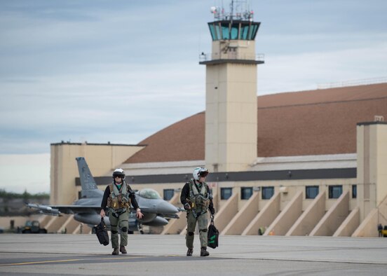 Two Royal Canadian Air Force CF-18 Hornet aircraft pilots assigned to the 409th Tactical Fighter Squadron, Canadian Forces Base Cold Lake, Canada, walk from the Thunderdome, at Eielson Air Force Base, Alaska, Aug. 5, 2016, during the familiarization day of RED FLAG-Alaska (RF-A) 16-3, while a U.S. Air Force F-16 Fighting Falcon aircraft assigned to the 35th Fighter Squadron, Kunsan Air Base, Republic of Korea, taxis for take off. Free exchange of ideas between multilateral forces during RF-A enhances not just partners and sister-service relationships, but also their operational efficiency. (U.S. Air Force photo by Staff Sgt. Shawn Nickel)