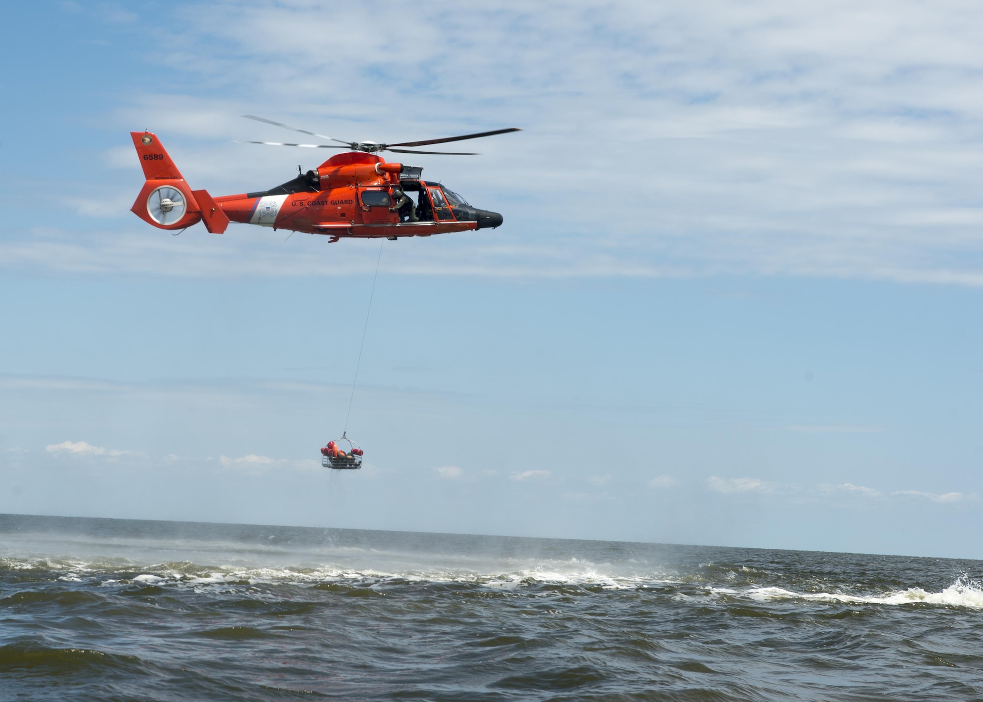 A Dover Air Force Base Airmen is basket lifted by a Coast Guard H-65 Dolphin helicopter during water survival training Aug. 6, 2015, Bower’s Beach, Del. Airmen with the 512th Airlift Wing and 436th Airlift Wing performed water survival training focusing on treading water, raft survival, and the basket lift helicopter evacuation. (U.S. Air Force Photo/ Tech. Sgt. Nathan Rivard)