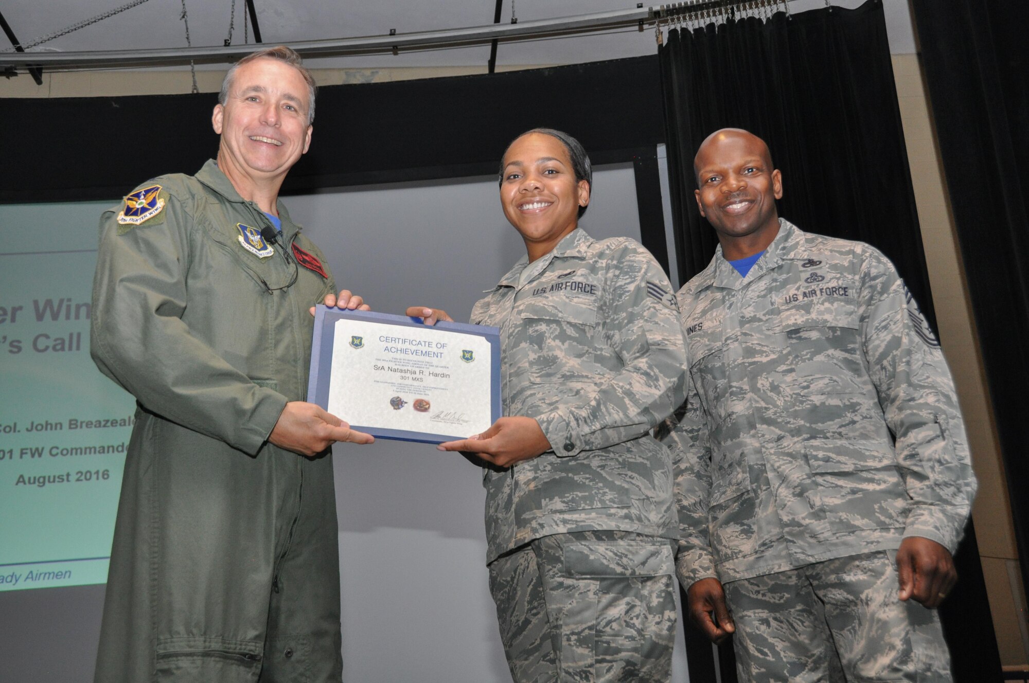 Col. John Breazeale, 301st Fighter Wing commander, and Chief Master Sgt. Terry Goines, 301st Fighter Wing command chief, are all smiles as they present a quarterly award to Senior Airman Natashja Hardin during a wing commander's call here Aug. 6. Hardin was recognized for her outstanding leadership, job performance, self-improvement and community involvement from April 1 - June 30, 2016. (U. S. Air Force photo by Capt. Candice Allen)