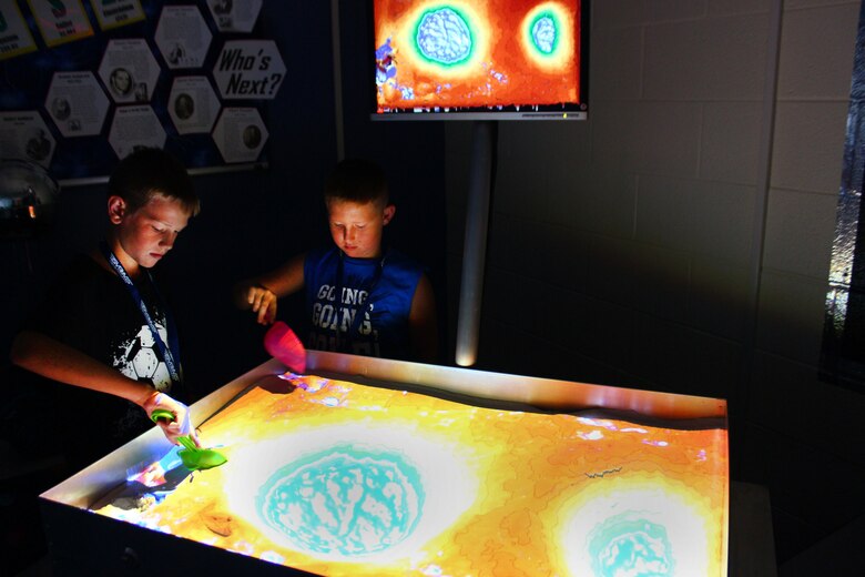 Colin Frye and Anderson Darby move sand around an augmented reality sandbox while attending a week-long STEM-based camp hosted by STARBASE Martinsburg, July 29 at the 167th Airlift Wing. The AR sandbox, the newest tool in the STARBASE Martinsburg classroom, allows users to create topography models by shaping real sand, which is then augmented in real time by an elevation color map, topographic contour lines, and simulated water. (U.S. National Guard photo by  Christopher Fleming)