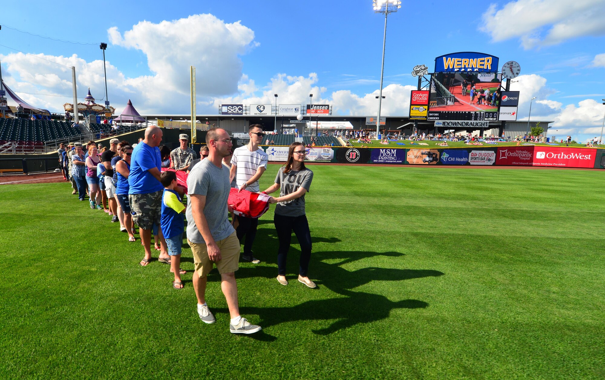 A combination of Airmen, Soldiers and dependents walk a giant-sized United States flag to centerfield of Werner Park in Papillion, Neb. Aug. 7, home of the Omaha Storm Chasers, during a military appreciation game. The Storm Chasers are the Triple-A affiliate of the Kansas City Royals.  (U.S. Air Force photo by Josh Plueger)