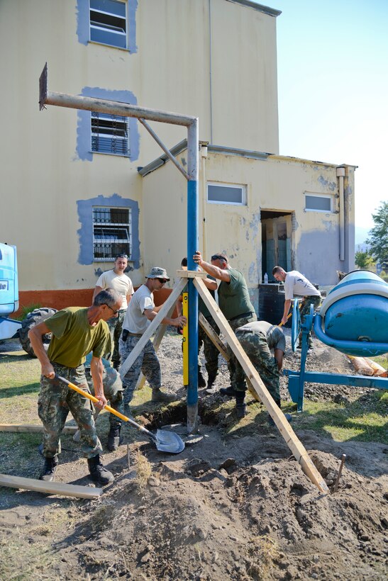 U.S. Air Force Senior Master Sgt. Todd Butcher, civil engineer with the New Jersey Air National Guard, holds a level while Albanian Army soldiers from the 1st Infantry Battalion of the Albanian Land Forces steady a pole for a basketball hoop and shovel concrete into the hole at a local school near Vau i Dejës, Albania on July 13, 2016. Civil engineers from the 177th Fighter Wing worked with the Albanian military members on Humanitarian and Civic Assistance projects during their two week long deployment for training, which included plumbing, electrical, ceramic tile, roofing, and door and frame maintenance and installations at a medical clinic. New Jersey and Albania are paired under the National Guard's State Partnership Program and are a proven partnership built upon shared values, experiences and vision. (U.S. Air National Guard photo by Master Sgt. Andrew J. Moseley/Released