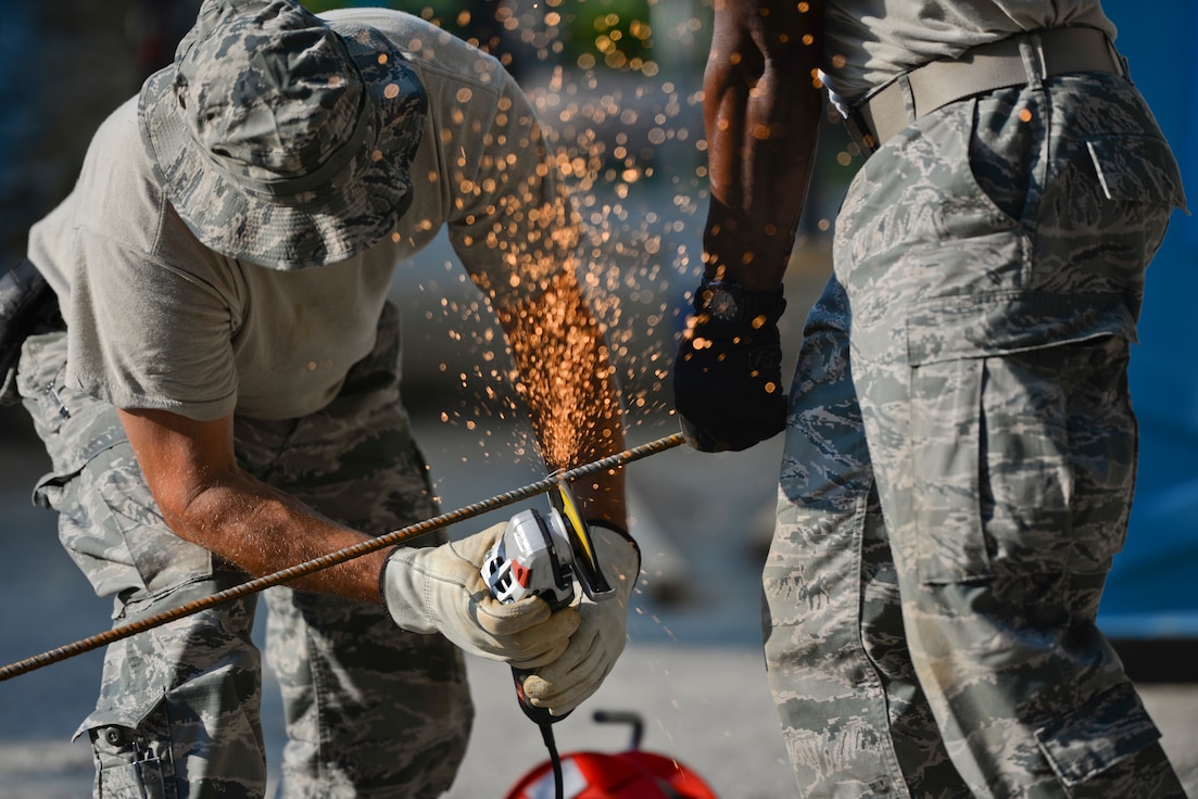 U.S. Air Force Senior Master Sgt. Todd Butcher, New Jersey Air National Guard civil engineer, uses an angle grinder with an abrasive disc to cut a reinforcing bar held by Master Sgt. Delroy Wallace in Vau i Dejës, Albania on July 11, 2016. The 177th Fighter Wing civil engineers were working on Humanitarian and Civic Assistance renovation projects at a local medical clinic during their two week long deployment for training. New Jersey and Albania are paired under the National Guard's State Partnership Program and are a proven partnership built upon shared values, experiences and vision. (U.S. Air National Guard photo by Master Sgt. Andrew J. Moseley/Released)