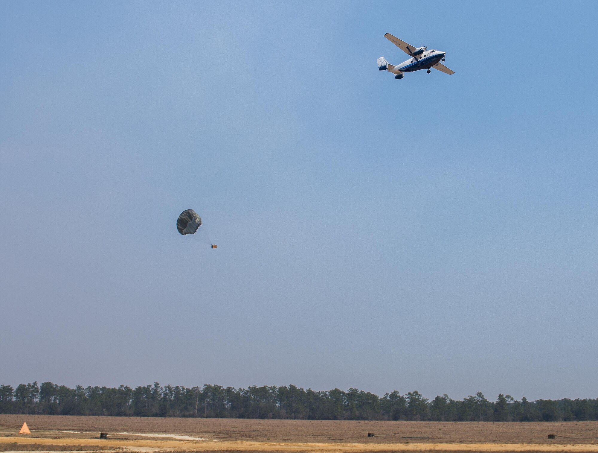 A parachuted bundle soars out of the back of a C-145 Skytruck during an airdrop mission over the Eglin Air Force Base range.  New and prior-qualified loadmasters release sandbags and 300-pound boxes from the 919th Special Operations Wing aircraft to as part of their initial airdrop or proficiency training.  The 919th Special Operations Logistics Readiness Squadron’s Airmen are responsible for packing, securing and recovering the equipment and parachutes.  (U.S. Air Force photo/Sam King)  