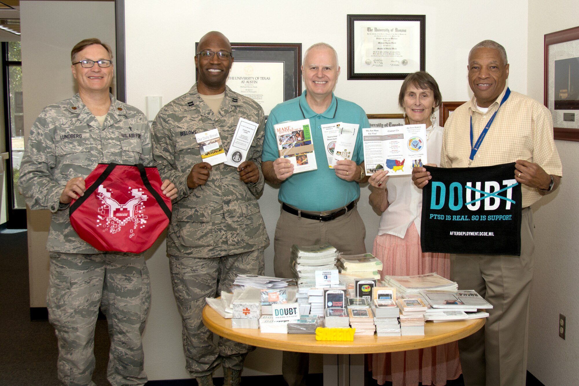 The 349th Air Mobility Wing's "helping agencies" stand with swag bag items such as psychological health pamphlets and deployment assistance cards on Aug. 8, 2016 at Travis Air Force Base, Calif. 349th AMW chaplains Maj. Glenn Lundberg and Capt. Kemuel Bellows, Dr. Michael Slack, 349th AMW Director of Psychological Health, Karen Orcutt, Psychological Health Advocacy Program case facilitator, and Marcellus Cook, PHAP outreach specialist, worked together with Slack to collect the items and bags, which will be passed out by Slack and the chaplains during the August Wingman’s Days. (U.S. Air Force photos by Senior Airman Shelby R. Horn)