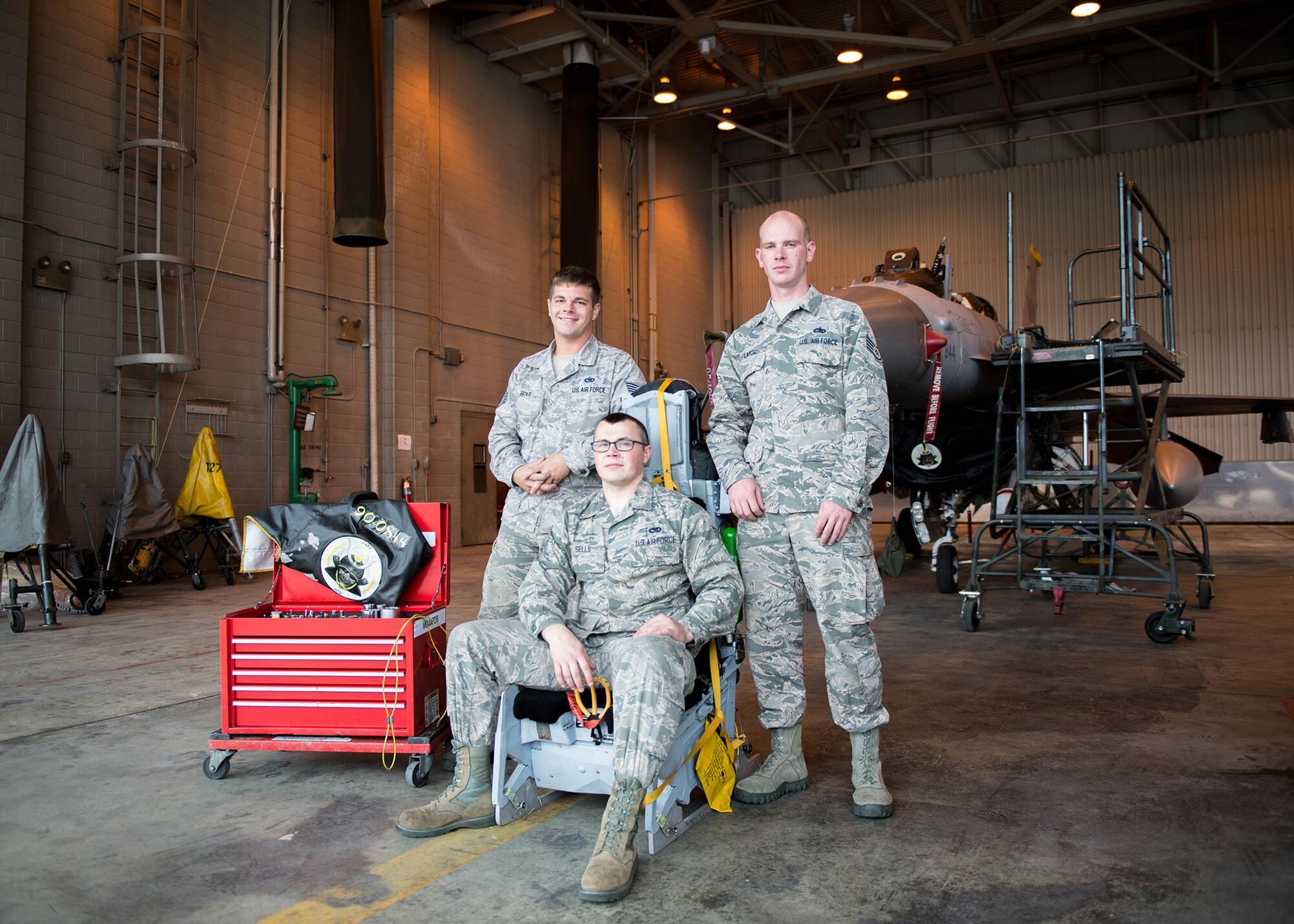 U.S. Air Force Staff Sgt. Corey Holt and Senior Airman Shane Sells, both assigned to the 8th Maintenance Squadron, Kunsan Air Base (AB) Republic of Korea, and Staff Sgt. Corey Holt, assigned to the 35th Maintenance Squadron, Misawa AB, Japan, all aircrew egress systems technicians, work together to install an ejection seat that was proving to be difficult to bolt-in on an F-16D Fighting Falcon aircraft Aug. 9, 2016, during RED FLAG-Alaska 16-3 at Eielson Air Force Base, Alaska. By working together, even though they are from different bases in the Indo-Asia-Pacific, they saved 50 percent on man-hours and sharpened their combat skills by working in the exercise aimed at creating a realistic threat environment at simulated forward operating bases. (U.S. Air Force photo by Staff Sgt. Shawn Nickel)